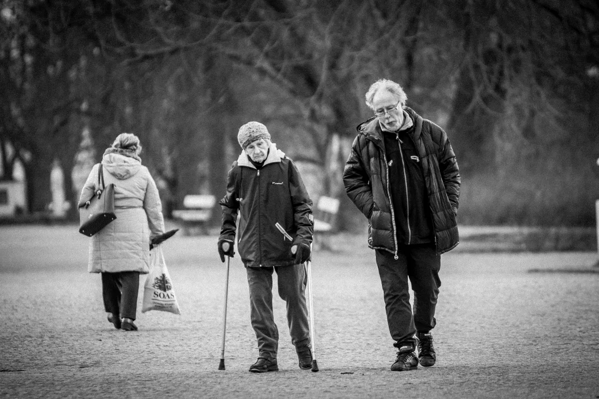 Woman with a cane walking beside an older man while another woman walks away